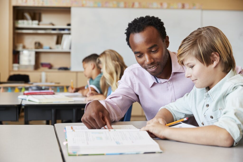 Teacher working with elementary school boy at his desk