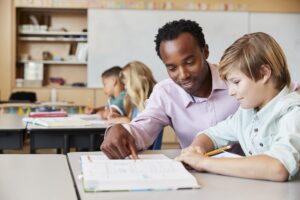 Teacher working with elementary school boy at his desk